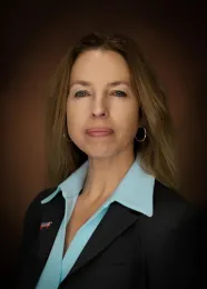 A headshot of Kim Brackett in a dark jacket and aquamarine shirt.