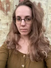 A woman wearing glasses and a brown shirt, and a tan background