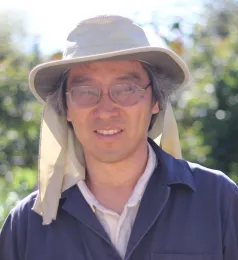 A man with glasses and a dark blue jacket, with a blurred background