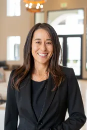 A woman in a black suit, with a tan background