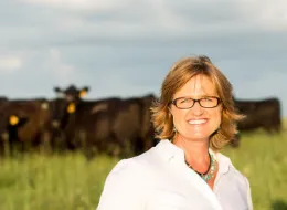 Debbie Lyons-Blythe in a pasture with cows behind her.