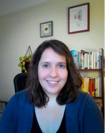 A woman in a blue shirt, with a bookshelf in the background