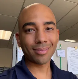 A man in a dark blue shirt, with an office in the background