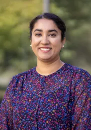 A woman in a purple floral blouse and a blured backdrop of trees and green foliage
