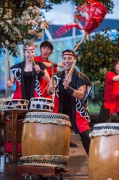 Young people dressed in black and red drumming on Japanese drums.