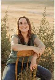 Youth member smiling while sitting with hands resting, with a valley landscape in the background.