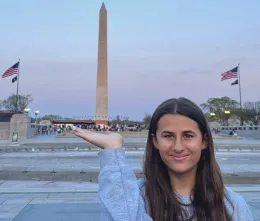 A 4-H youth stands in Washington, D.C., holding their hand up toward a tower.