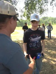A 4-H youth receives an award from a volunteer at an archery competition.