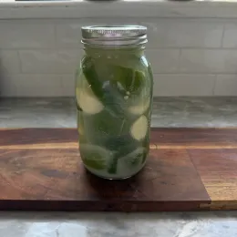 limes in a glass ball jar are fully submerged in the liquid