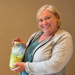 a smiling woman holding a half-gallon jar of homemade sauerkraut