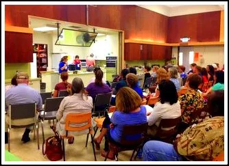 The room is filled with people facing the kitchen area, where the UC Master Food Preservers of Sacramento County host a pickle-making demonstrration. 