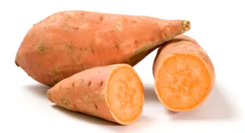 Two orange sweet potatoes on a white background, one cut in half to show its bright orange flesh.