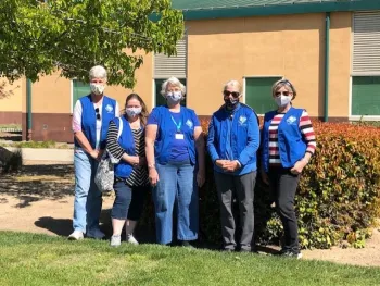 5 members of the sensory garden committee are standing and smiling (while wearing masks) at the site of the upcoming garden.