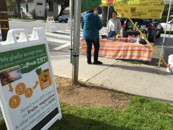 A farmers market manager booth with a sign in front that says CalFresh accepted here