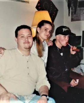 Three teens pose for a photo. The teen on the far right has a lollipop in his mouth.