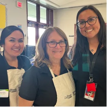 Sue Lafferty, wearing a white apron, stands between 2 women