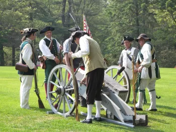 A group of men gather around a catapult for a revolutionary war reenactment. 