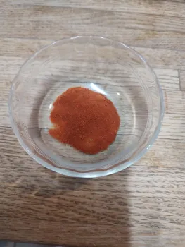 Small glass bowl on a table with red tomato powder in it. 
