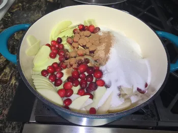 Pot on the stove filled with sliced apples, pears, cranberries, sugar, and spices. 