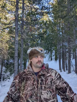 Bob is standing on snow-covered ground surrounded by tall evergreen trees
