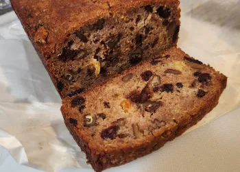 A close-up view of a loaf of fruit and nut bread on parchment paper