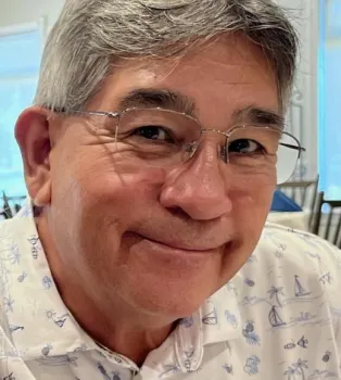 Close-up image of a man, smiling and wearing glasses