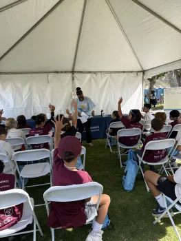 Instructor engaging with elementary students during a hands-on water treatment demonstration under a tent.