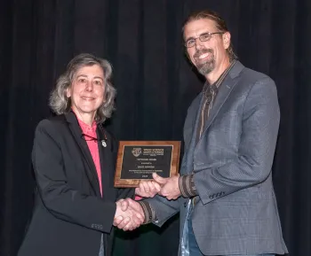 A woman hands Brad a plaque and shakes his hand