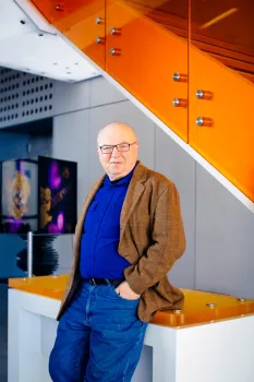 Zilberman stands with hands in his pants pockets and leans back on an orange table