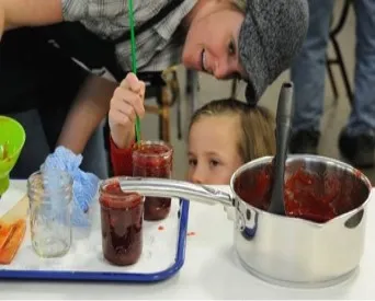Woman helping small child measure headspace in a jar of jam