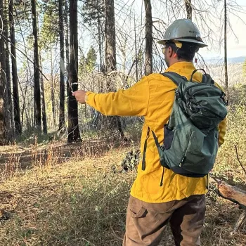 A person monitoring weather conditions during a prescribed burn. They are swinging a sling psychrometer.