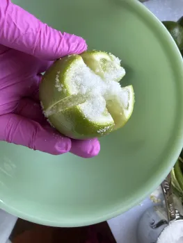  gloved hand holds a quartered lime covered in salt over a bowl