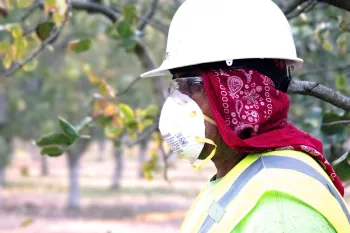 an agricultural worker in proper PPE (mask, goggles, etc.) stares into the distance