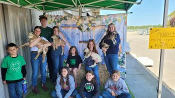 4-H youth some holding lambs pose in front of a country barn door style backdrop