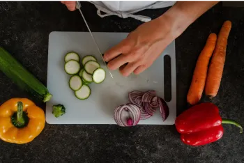 Hands chopping vegetables on a plastic cutting board.
