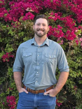 Chaydon shown waist up with hands in jeans pockets in front of a flowering bush