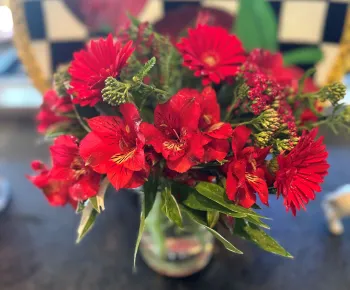 vase of red cut flowers including Gerbera daisies, Alstroemerias, and Achillia