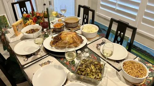 A dining table with stuffing, sweet potatoes, gravy, a roast turkey, mashed potatoes, Brussels sprouts, green bean casserole, and 5 glasses of wine.