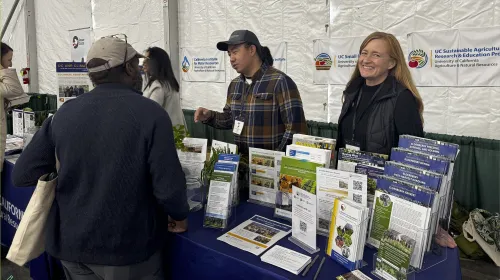 Two UC ANR representatives speak with an attendee during the EcoFarm 2026 conference.