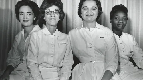 Three white women and one Black woman wearing white uniforms