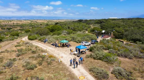 An aerial view of people standing under a tent in scrubland