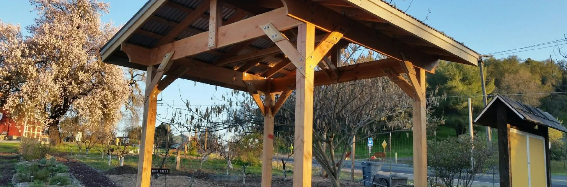 Open-walled wooden structure in the Demonstration Garden, with trees in the background.