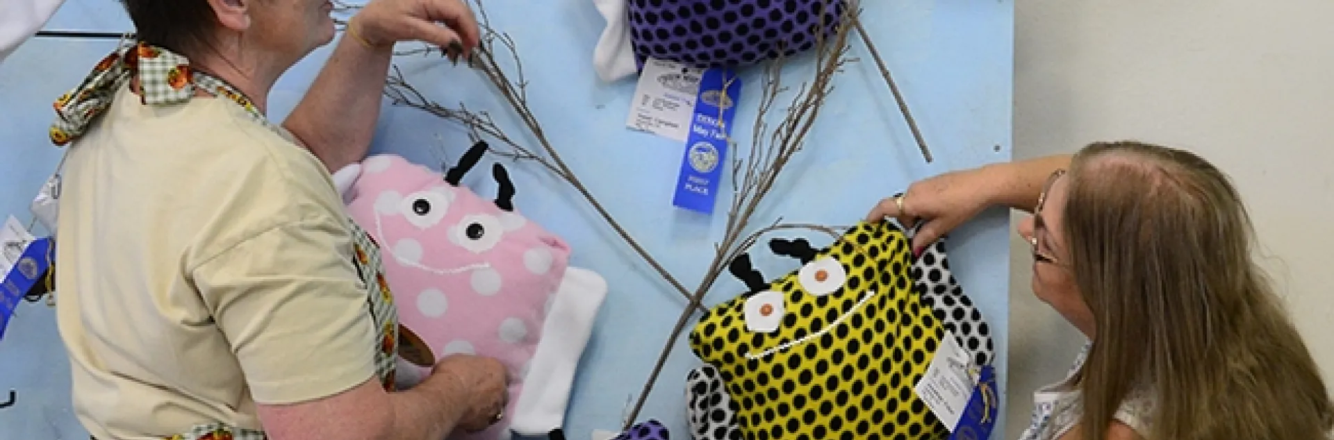 Dixon May Fair Youth Building superintendent Building superintendent Stephanie Hill (left) of Yuba City and assistant building superintendent Pat Connelly of Vacaville hang bumble bee pillow, the work of Solano County 4-H'ers. (Photo by Kathy Keatley Garvey)