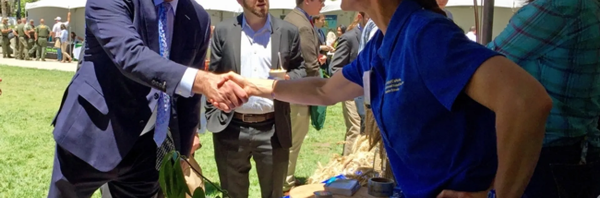 Assemblyman Gray, on left in navy-colored suit, shakes the hand of Michelle Leinfelder-Miles, who is wearing a blue ANR polo shirt.