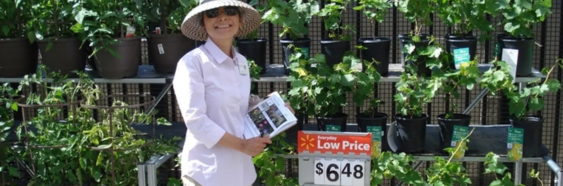 Woman with clipboard standing in front of a row of plants at a local nursery.
