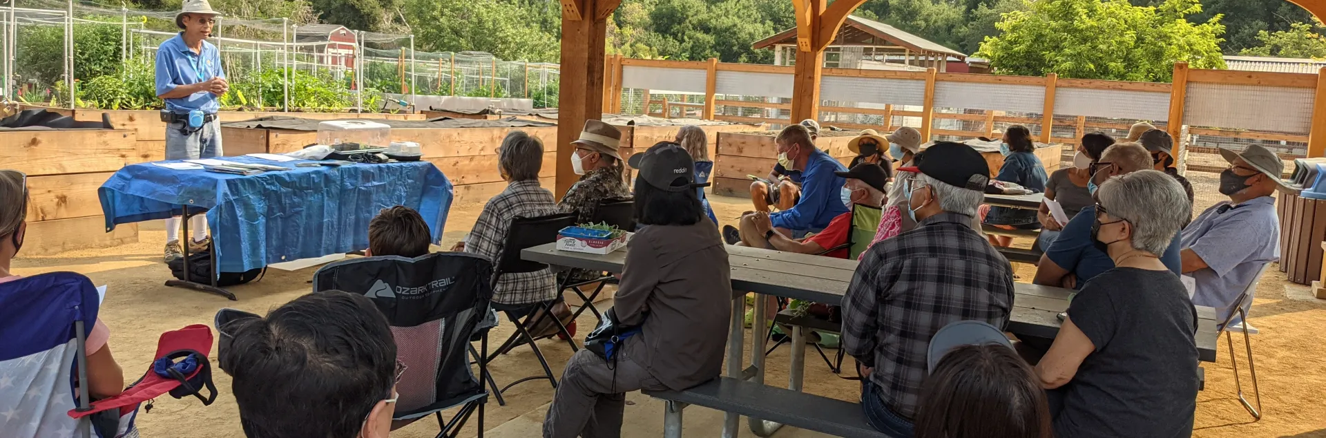 A man teaching a gardening class to a seated audience under a wooden pavilion at McClellan Ranch Preserve