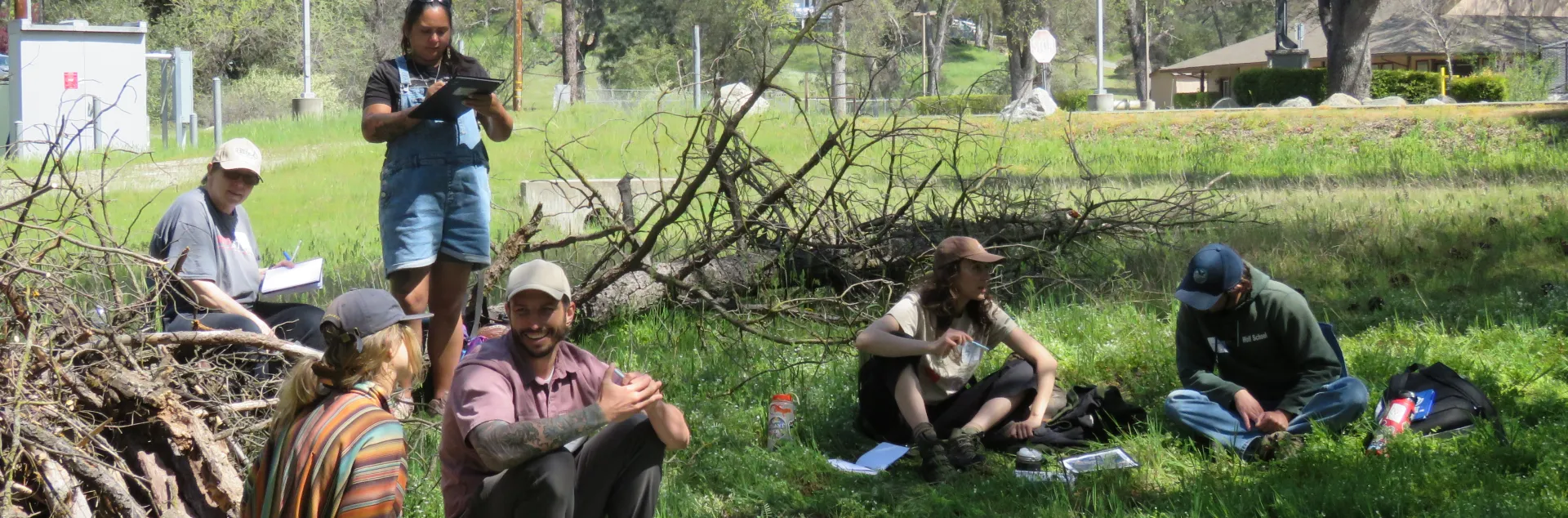 Group of people sitting and standing outside participate in a forestry class.