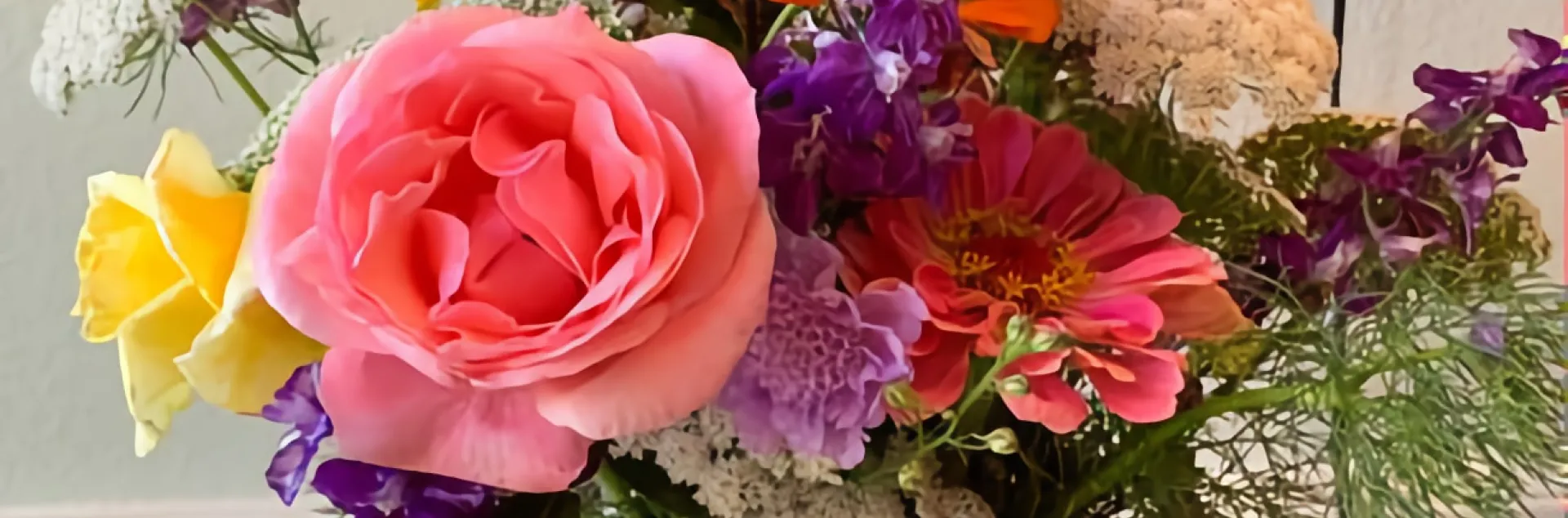 Cut flowers in a vase, including pink and yellow roses, orange zinnia, and purple larkspur