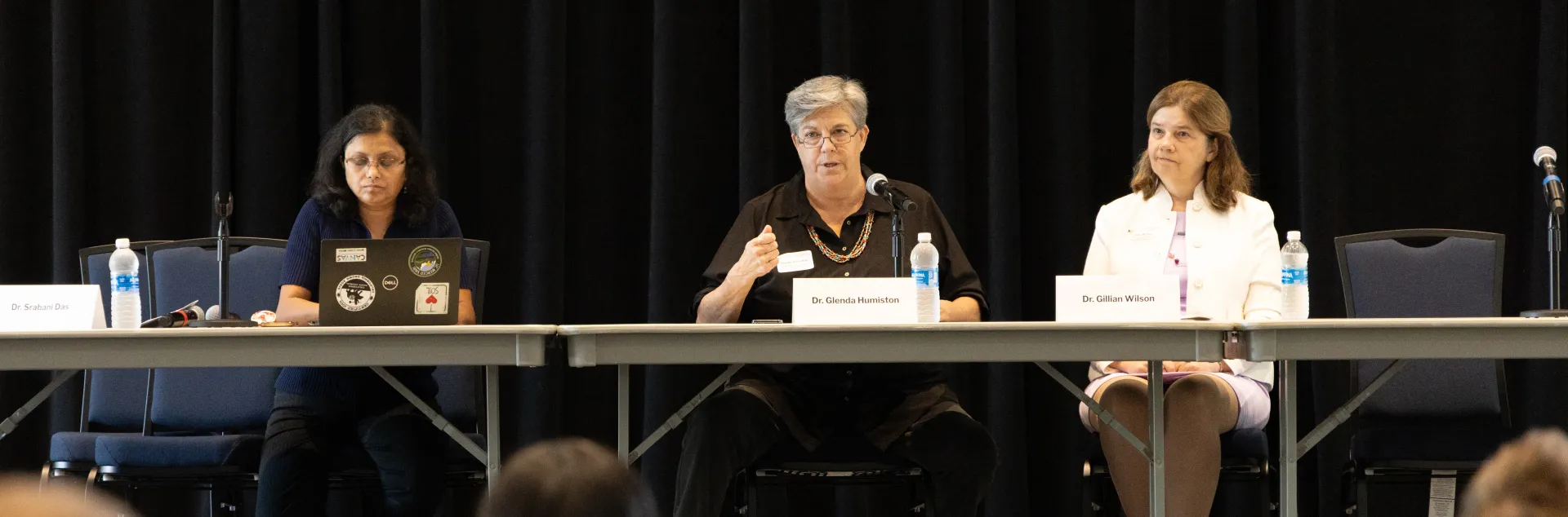 Srabani Glenda and Gillian sit at a long table facing the audience. Glenda is speaking into a mic