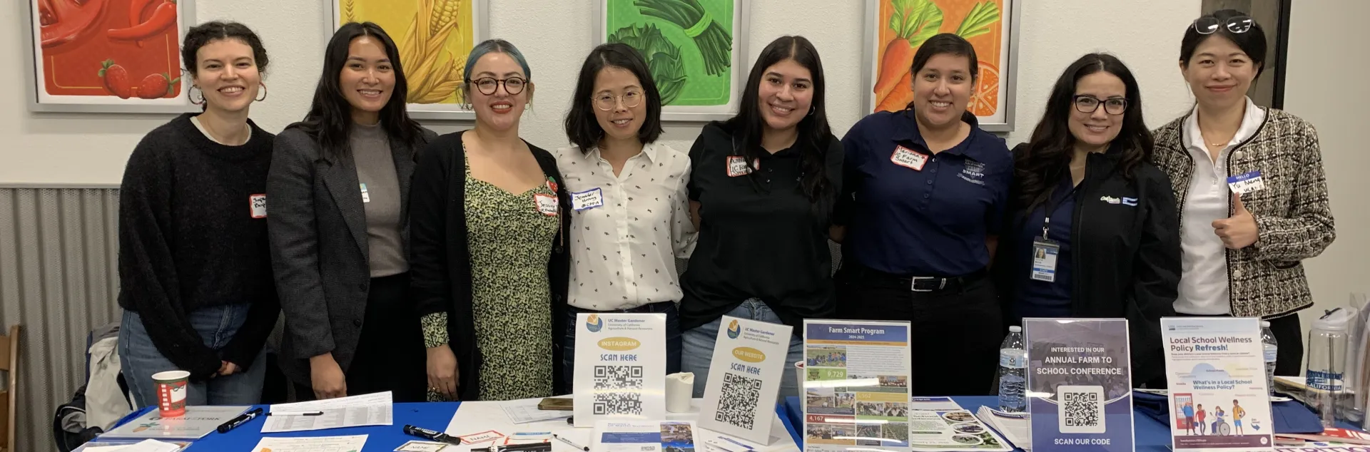 Eight women stand behind the Master Gardener and Farm Smart tables